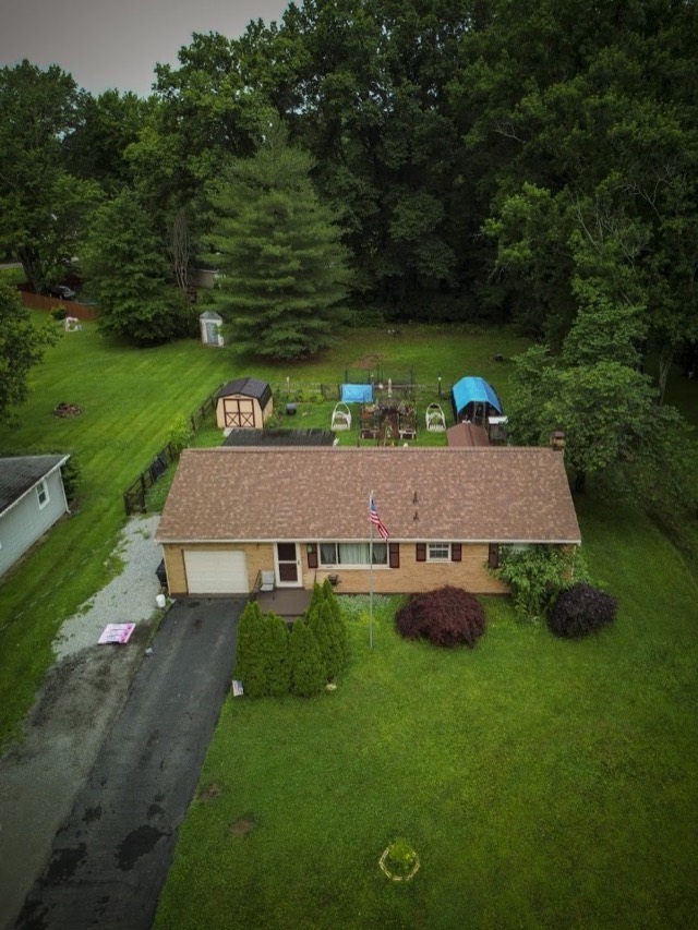 Ranch in a wooded yard: A brick ranch with a new brown shingle roof among mature trees.