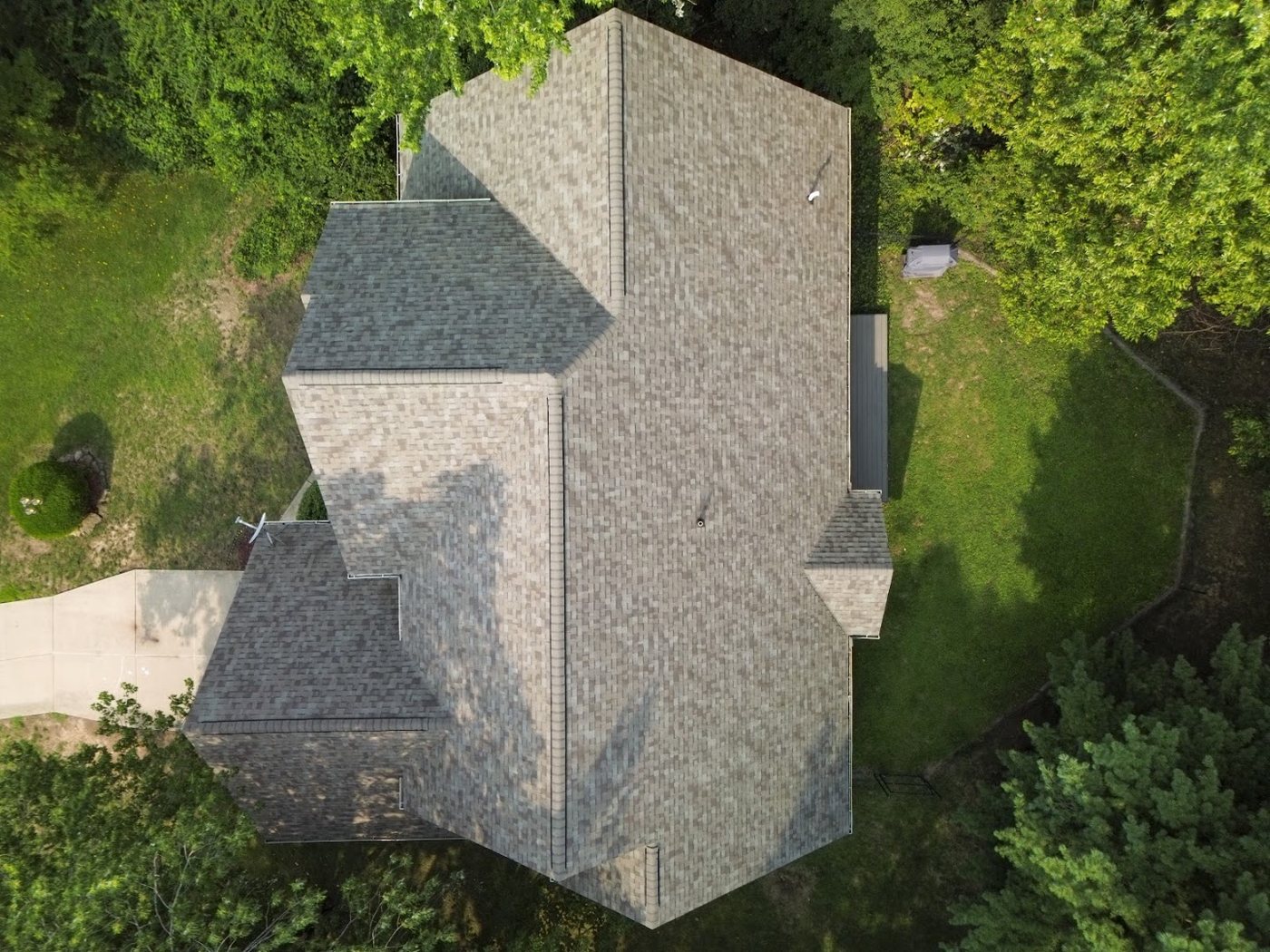 Aerial view of a complex grey shingle roof surrounded by mature trees